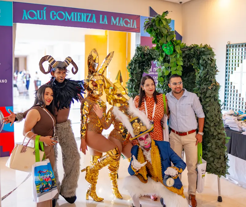 Personajes itinerantes dorados, con cuernos y de fantasía posando con asistentes bajo un arco que dice Aquí comienza la magia