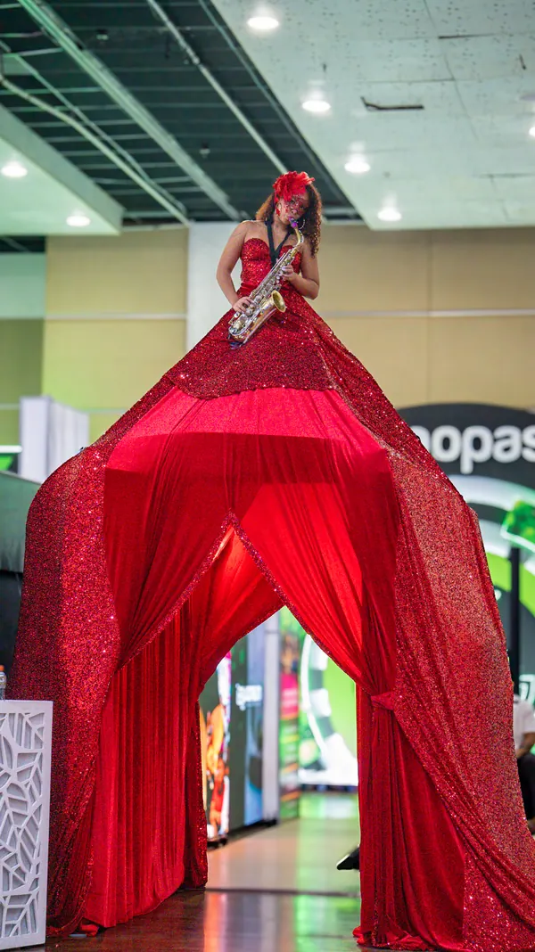 Mujer gigante tocando saxofón sobre un vestido rojo de lentejuelas que se abre como un túnel